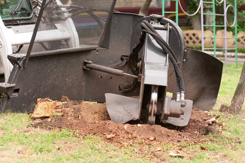 A black stump grinder machine grinding through the ground.