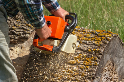 A man using an orange chainsaw to cut a piece of a tree trunk on the ground.